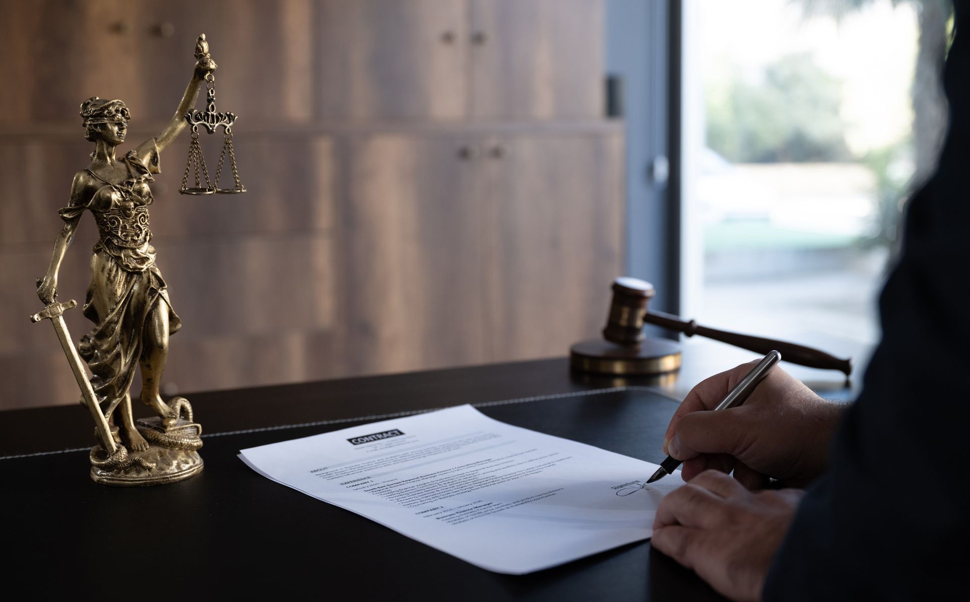 A person is signing a document in front of a statue of justice. A person is signing a document in front of a statue of justice.