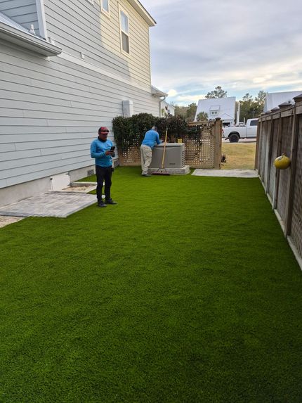 Person mowing a green lawn with a black push mower near a house