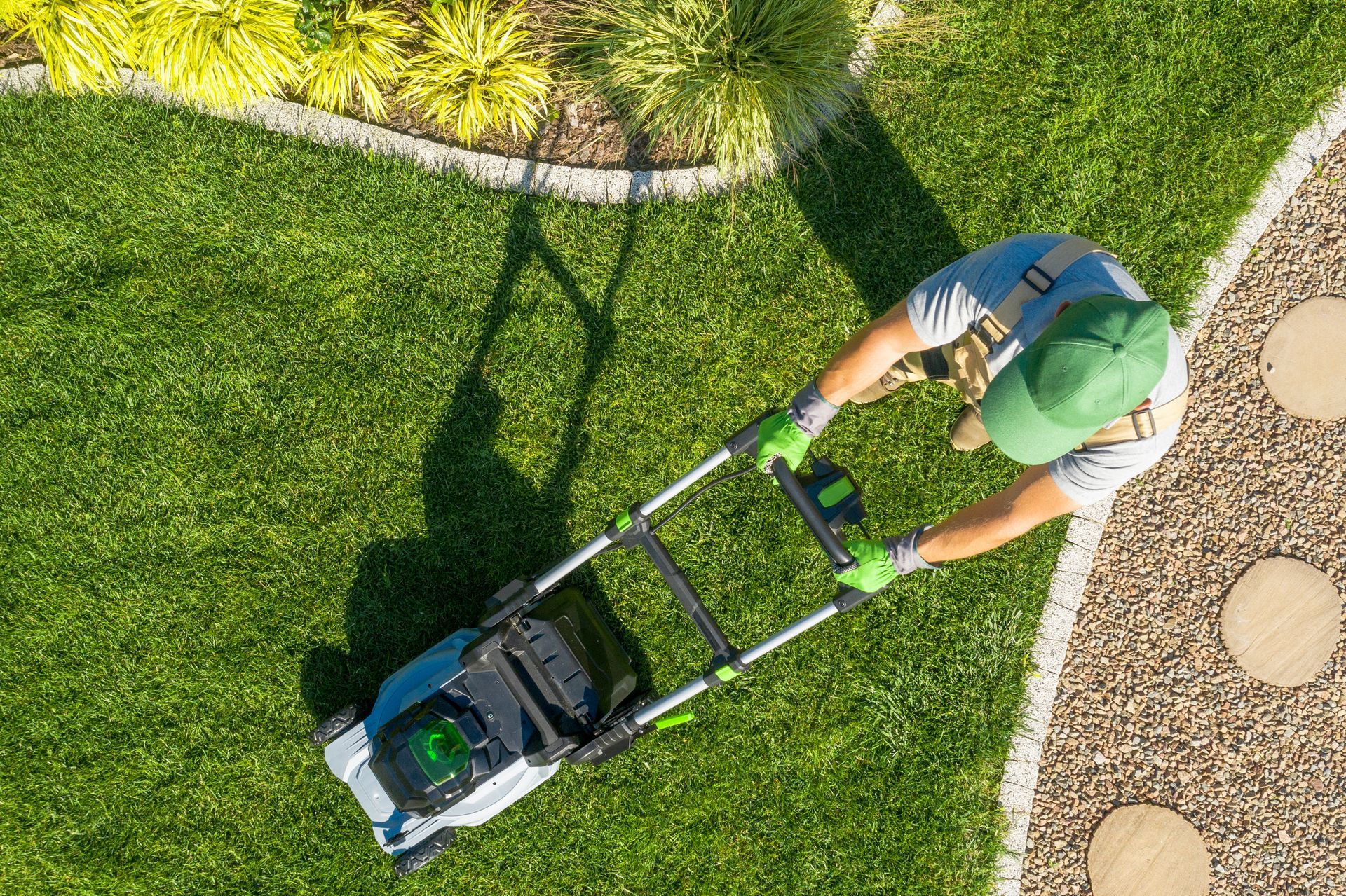 Person mowing a bright green lawn with a push mower, viewed from above.