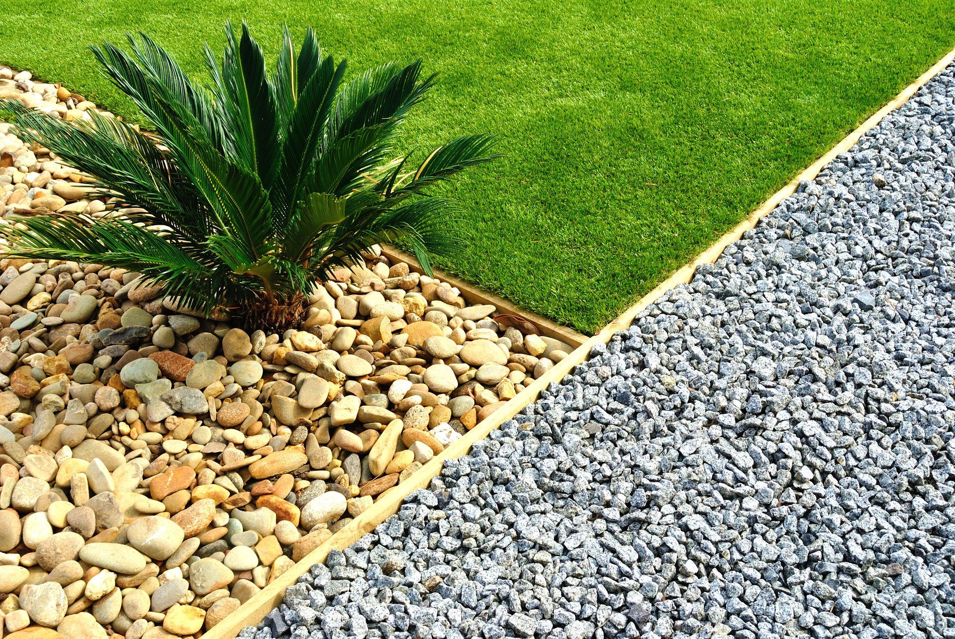 Decorative garden border with green grass, a small palm, and tan and gray gravel paths