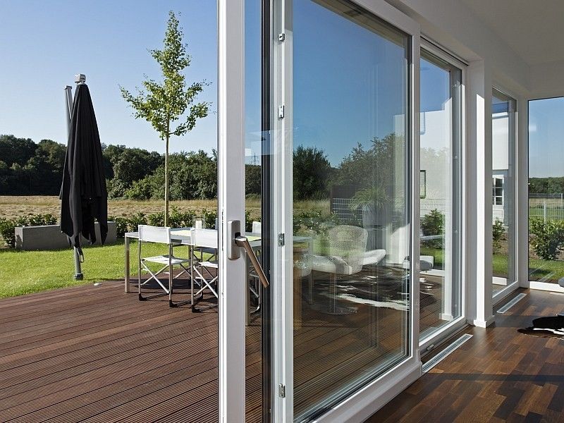 Le porte scorrevoli in vetro si aprono su una terrazza con mobili da esterno, che si affaccia su un prato soleggiato.
