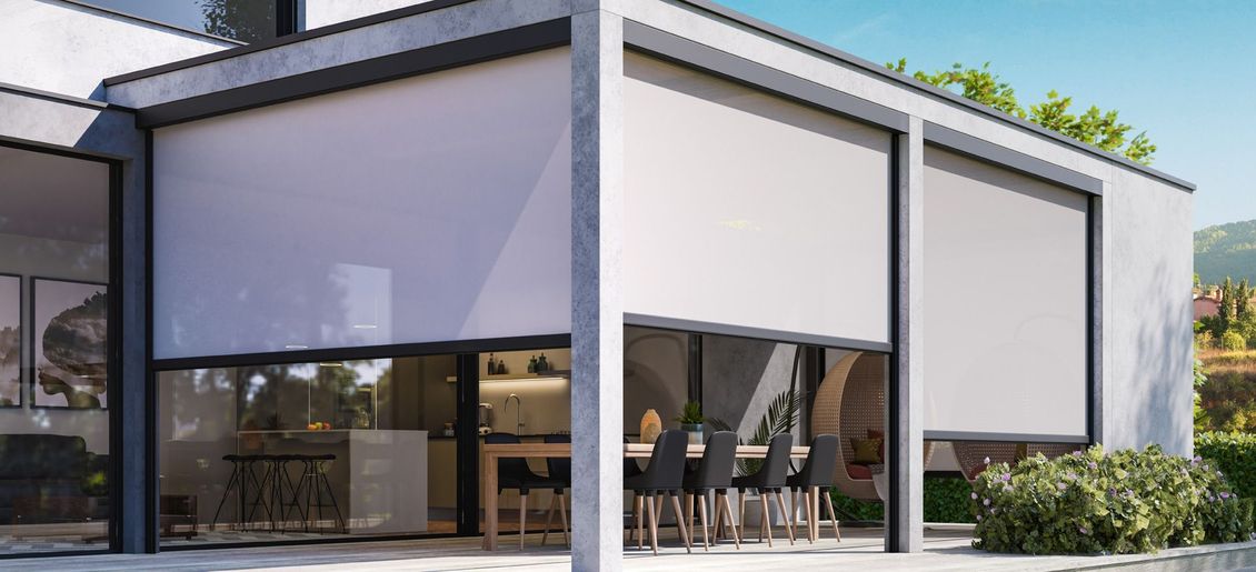Esterno di una casa moderna con tende da sole bianche che coprono parzialmente le grandi finestre e porte in vetro.