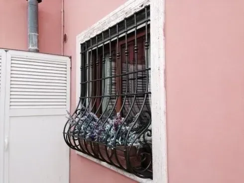 Esterno di un edificio rosa con finestra sbarrata e fioriera.