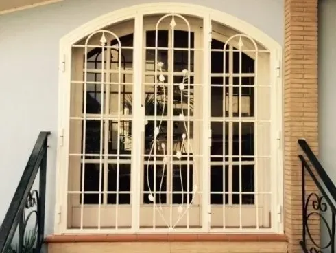 Porta di sicurezza in metallo bianco con parte superiore arcuata e motivo a griglia.