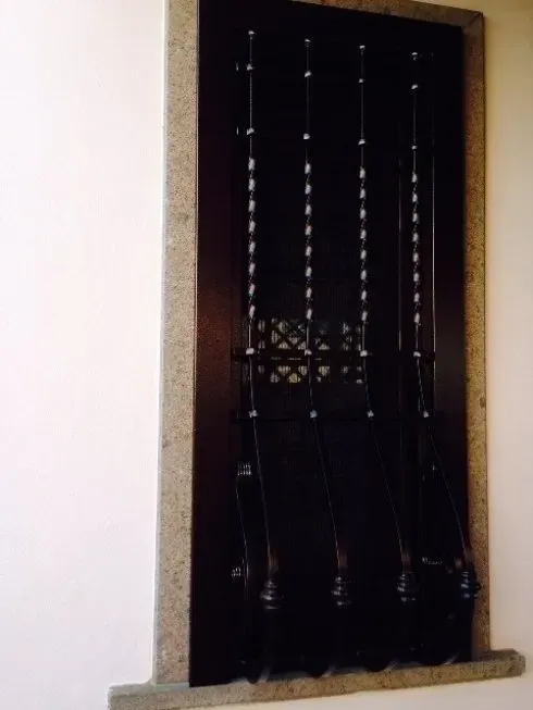 Finestra con cornice in legno scuro e inferriate decorative su una parete bianca.