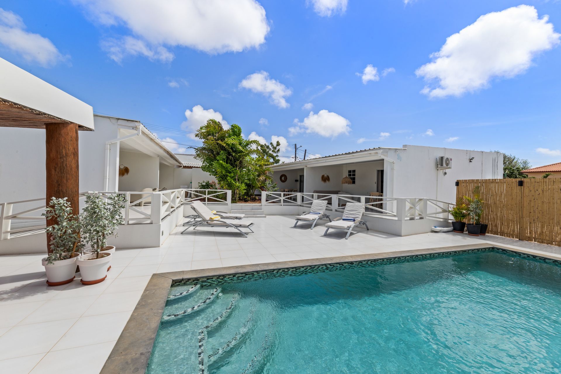 Pool with lounge chairs between two buildings, blue sky.