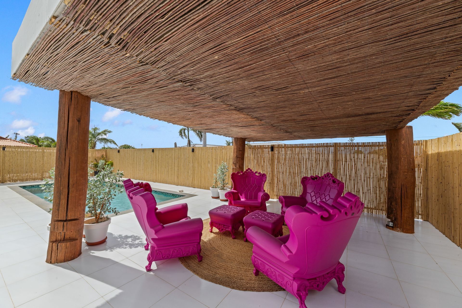 Poolside lounge area at night; illuminated pool, red furniture under pergola, string lights.