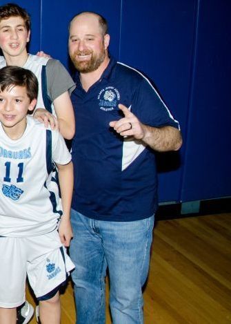 Man in navy shirt and jeans posing with two boys in basketball uniforms in a gymnasium