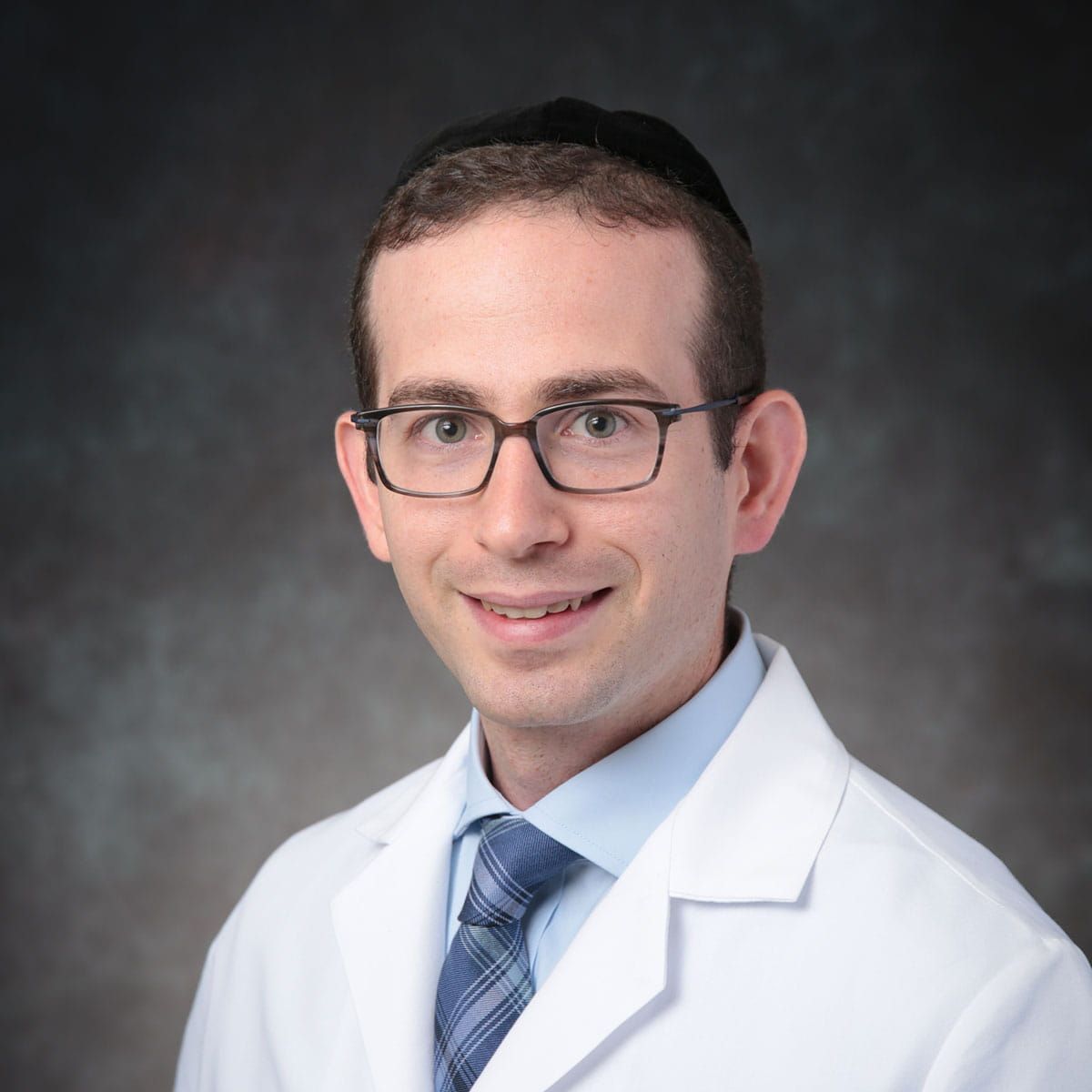 Portrait of a doctor in a white coat and glasses, smiling against a gray studio background
