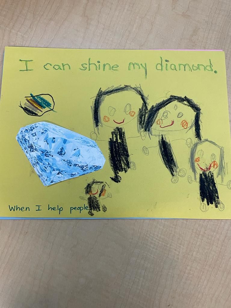 Child's crayon drawing on yellow paper with text, blue diamond shape, and three stick figures.