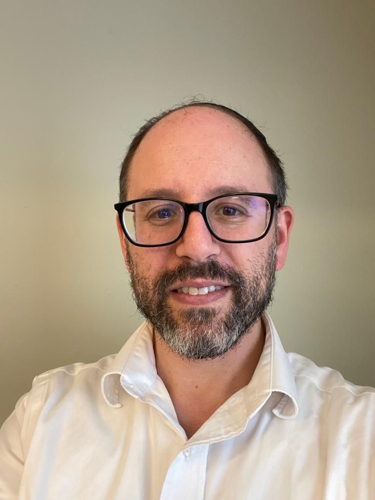 Smiling man with glasses and a beard in a white shirt against a plain background