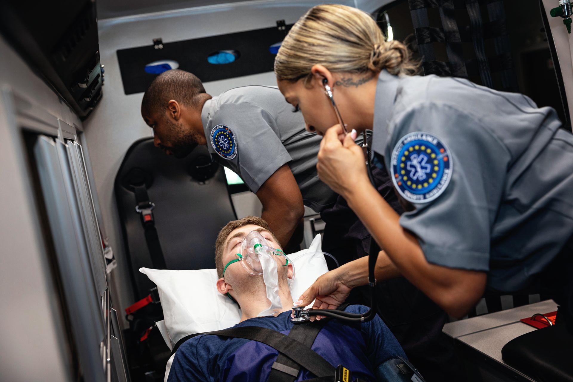 Emergency medical personnel tending to a patient on a stretcher inside an ambulance, using a stethoscope.