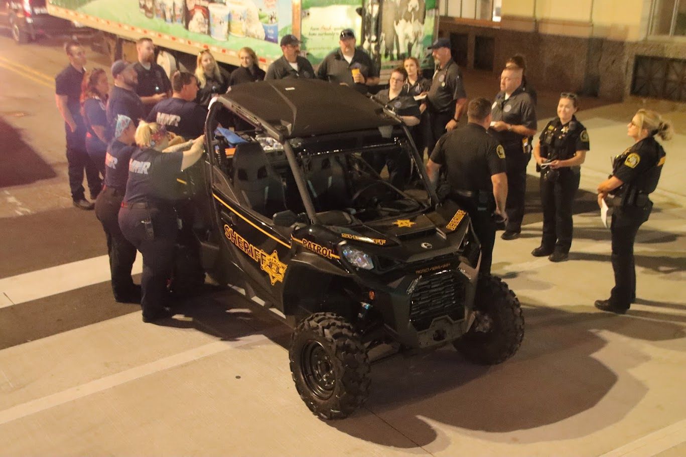 Group of officers around a black and green Sheriff's utility vehicle at night.