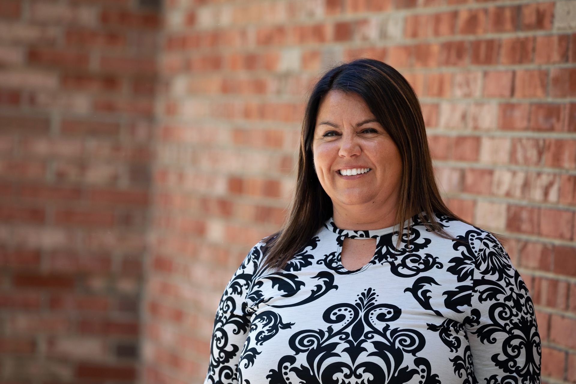 Woman in patterned top smiles in front of a brick wall.