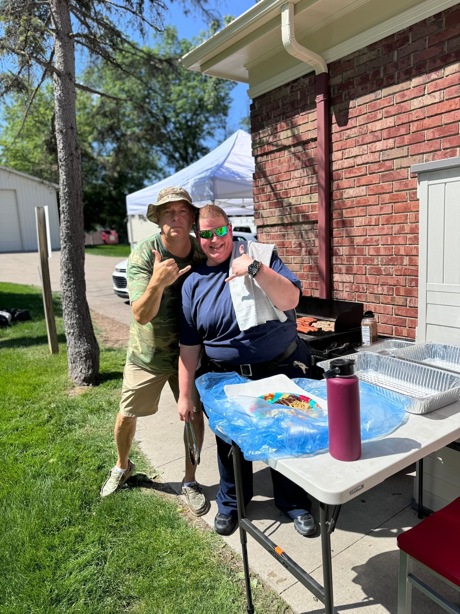 Two people smiling at a picnic table, one in camo giving a 