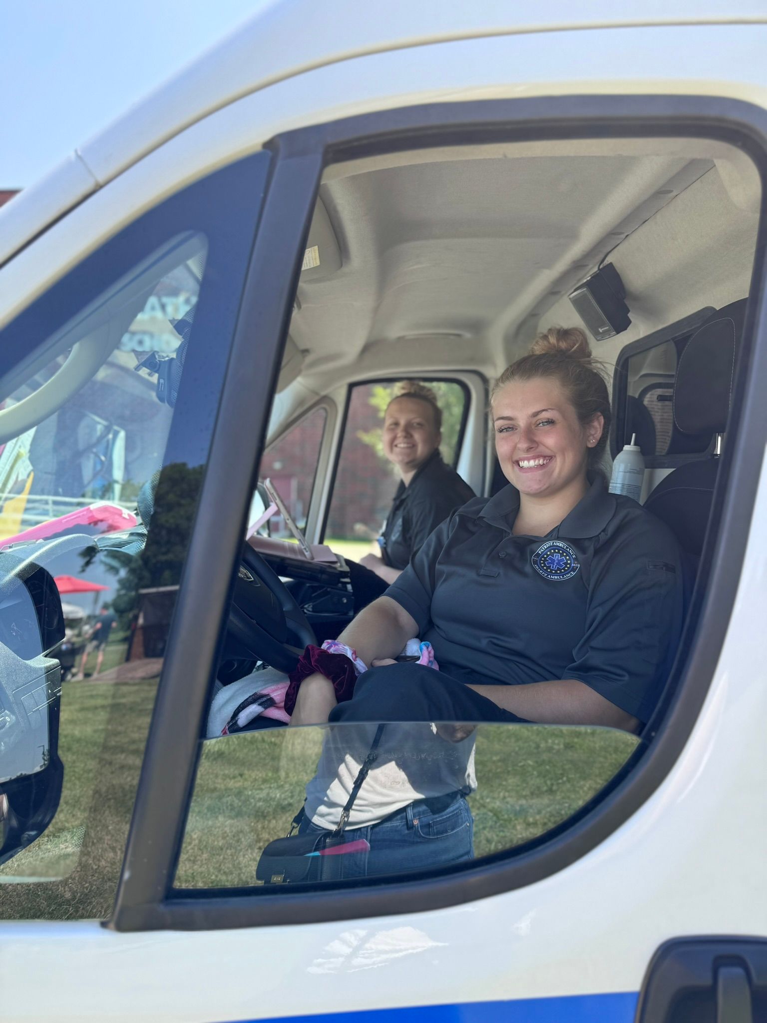 Two people smiling in a vehicle. One is driving, and the other is in the passenger seat.