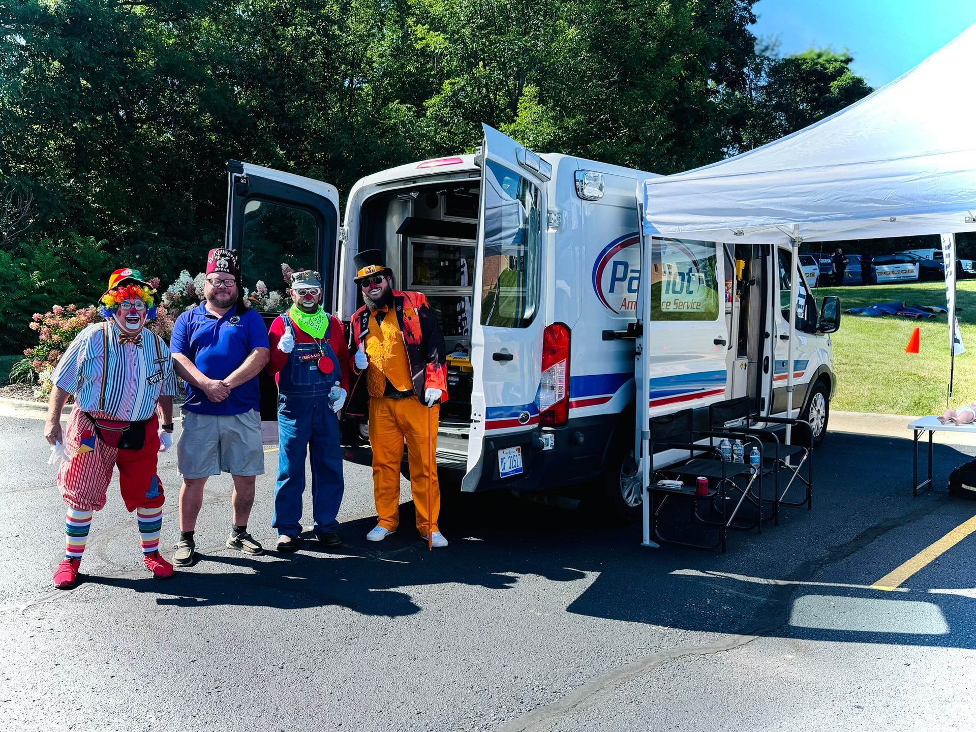 Clowns and others stand by a van with open doors and a tent. The van has a 