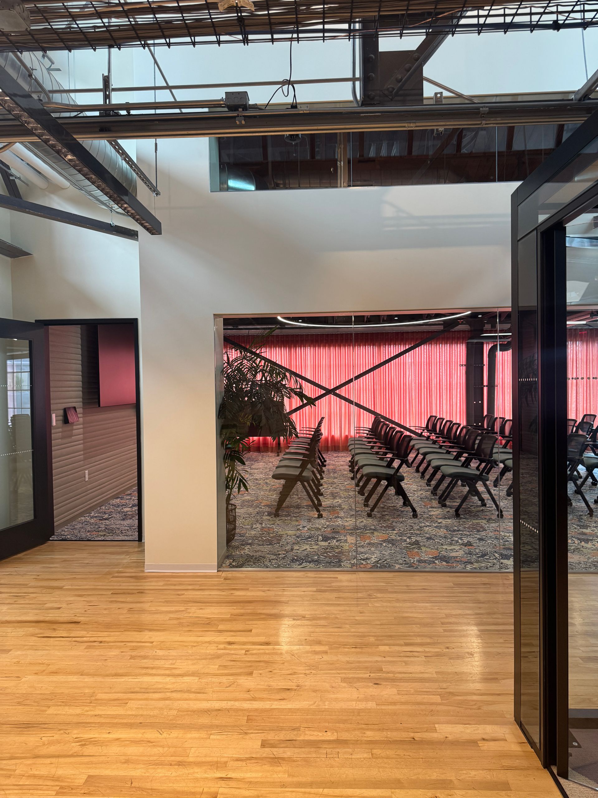 Wooden floored interior with a view into a room with chairs. Red curtains in the background.