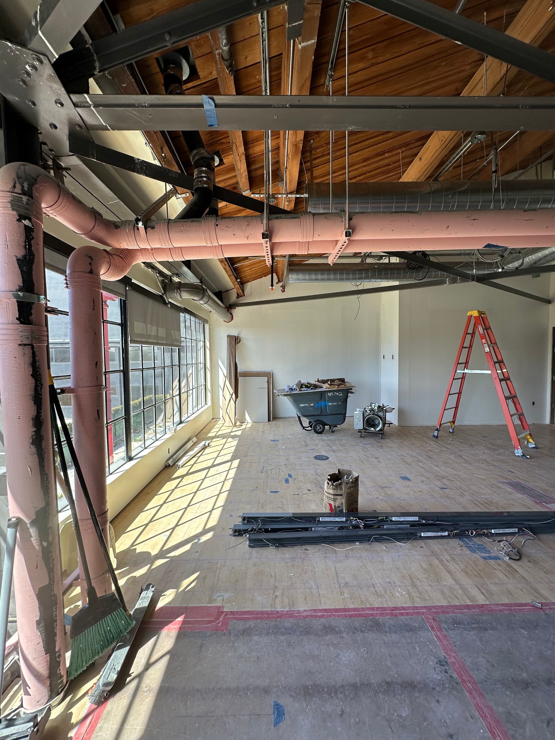Interior construction scene: exposed pipes, wood beams, and materials scattered on the floor.