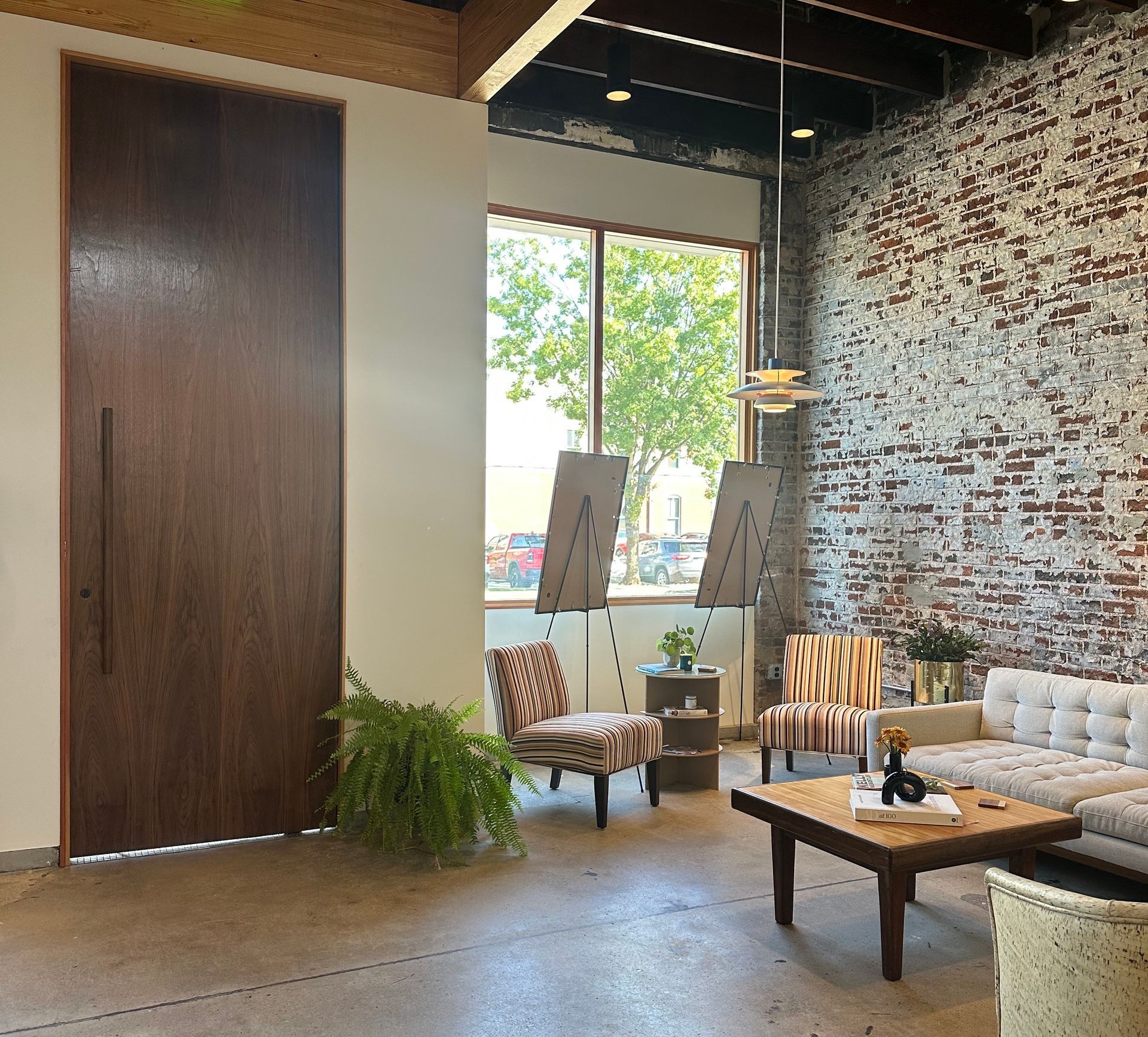 Living room with a brick wall, large wooden door, seating area and outdoor view.