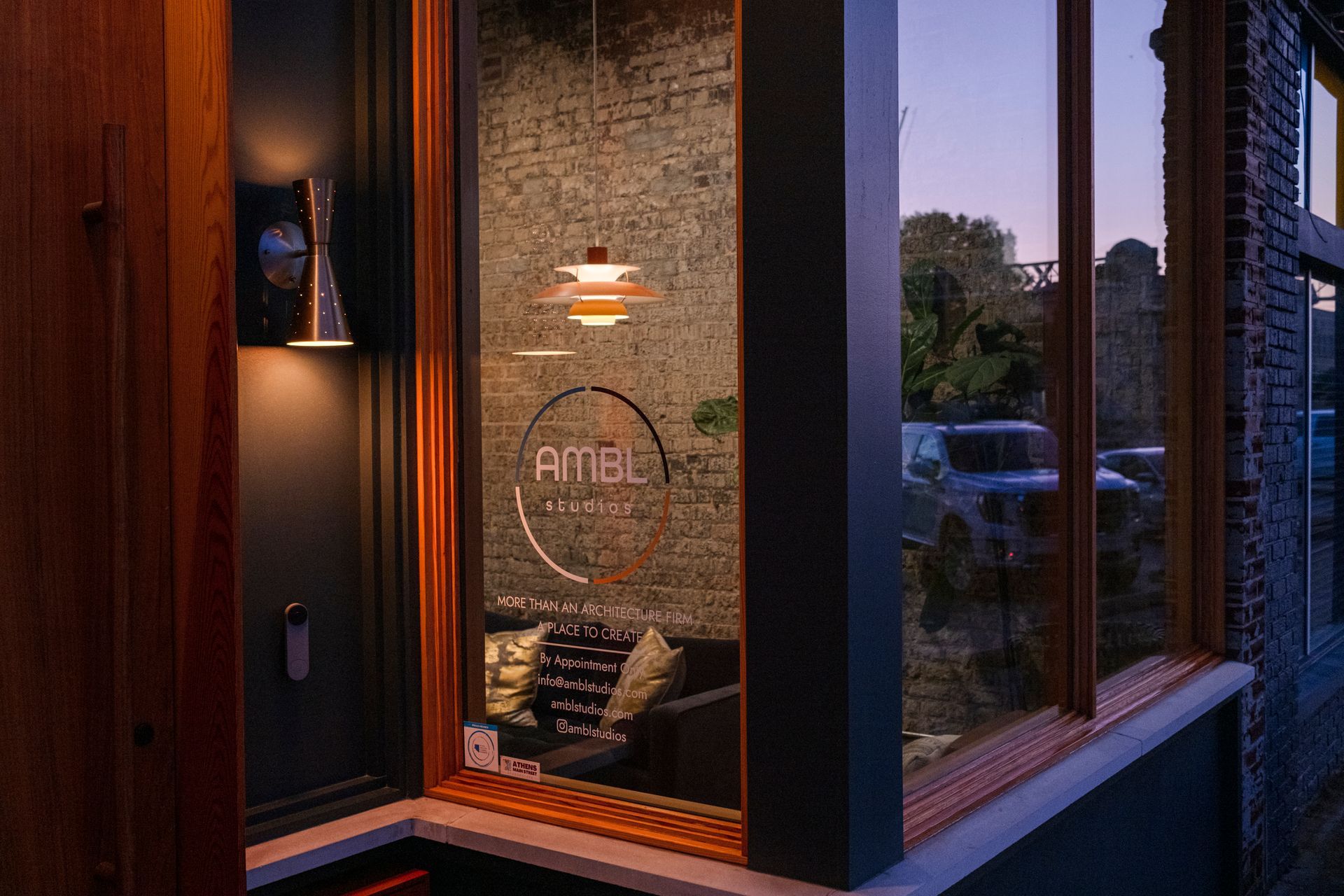 Exterior view of a shop window at dusk. Interior shows a waiting area with a logo.