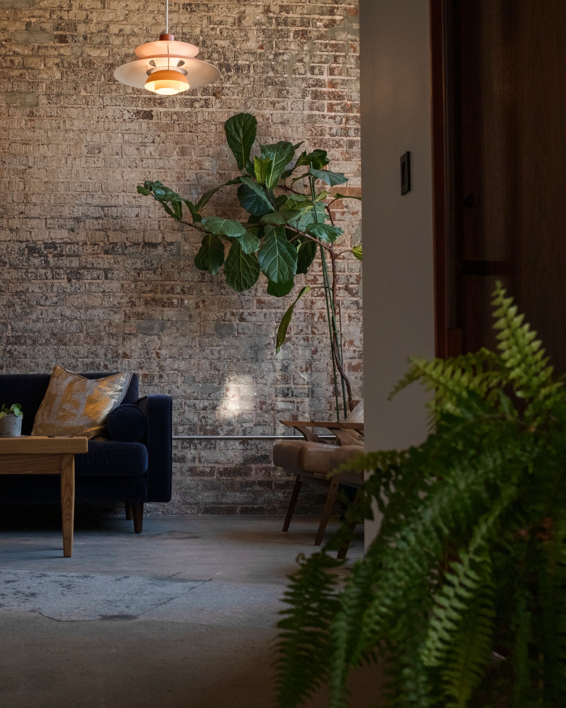 Living room with brick wall, sofa, plants, and wooden furniture.