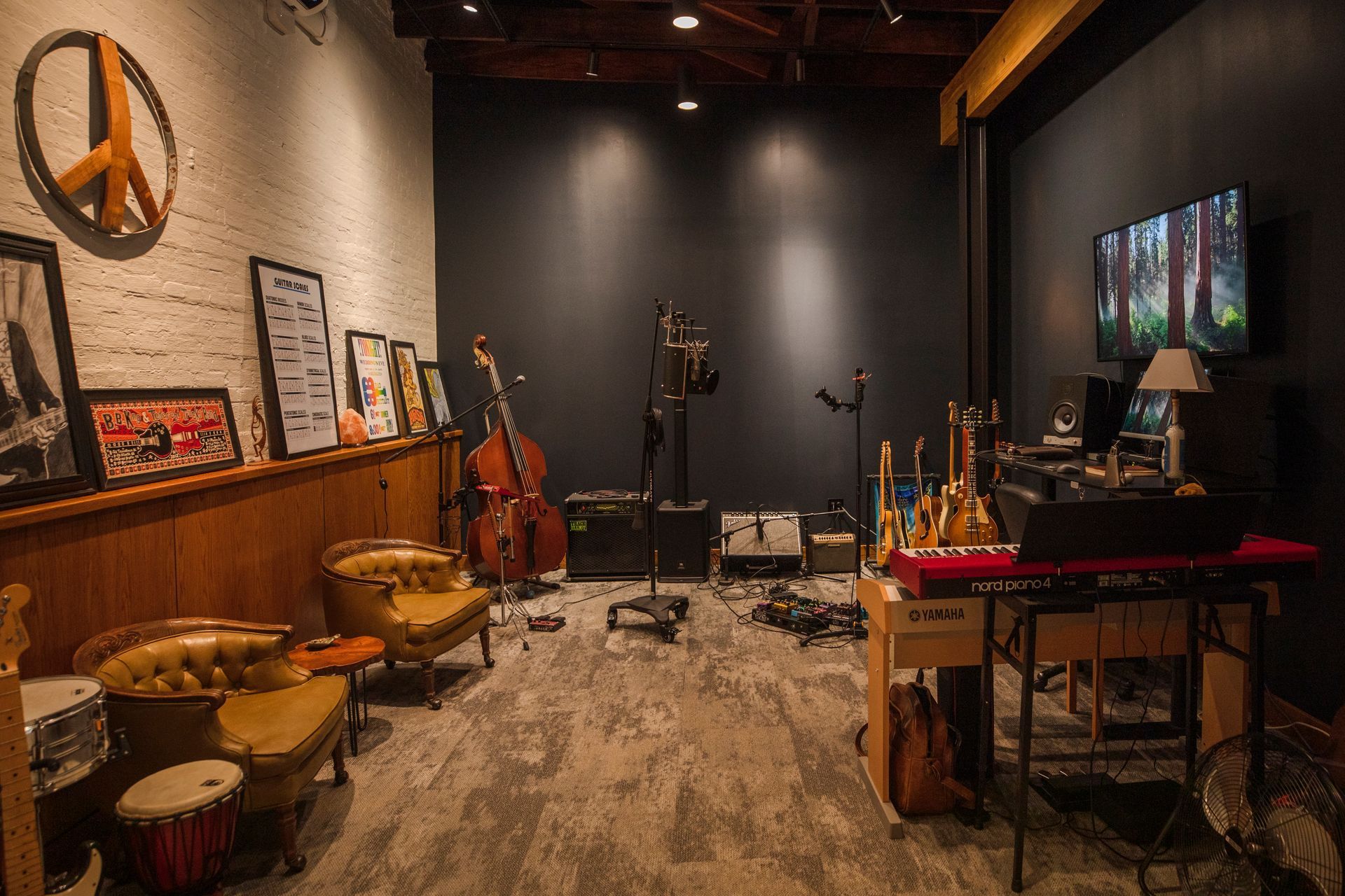 A music studio with instruments, seating, and a dark accent wall. Contains a television, framed art, and a peace sign.