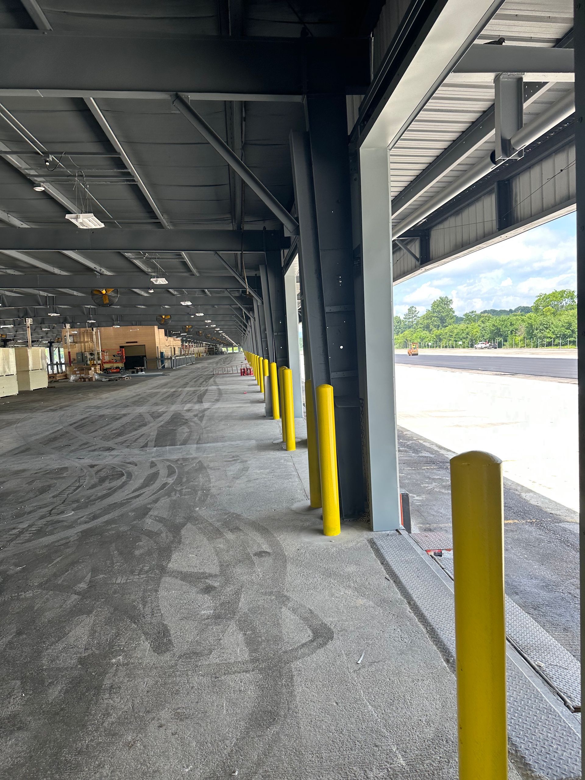 Covered warehouse loading dock with yellow bollards, gravel ground, and open side to bright outdoors.