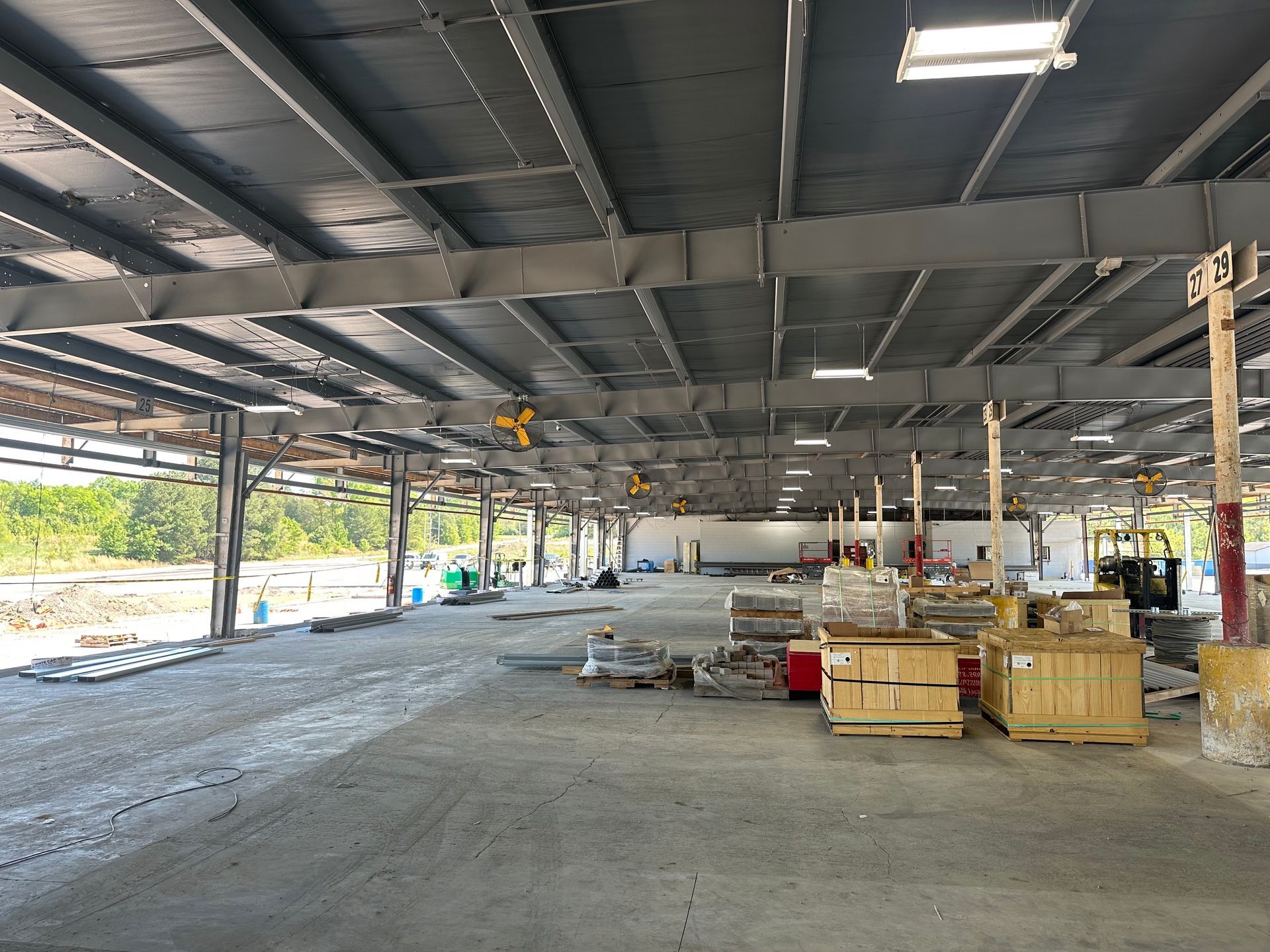 Large open warehouse interior with exposed steel beams, unfinished floor, and stacks of materials on the right.