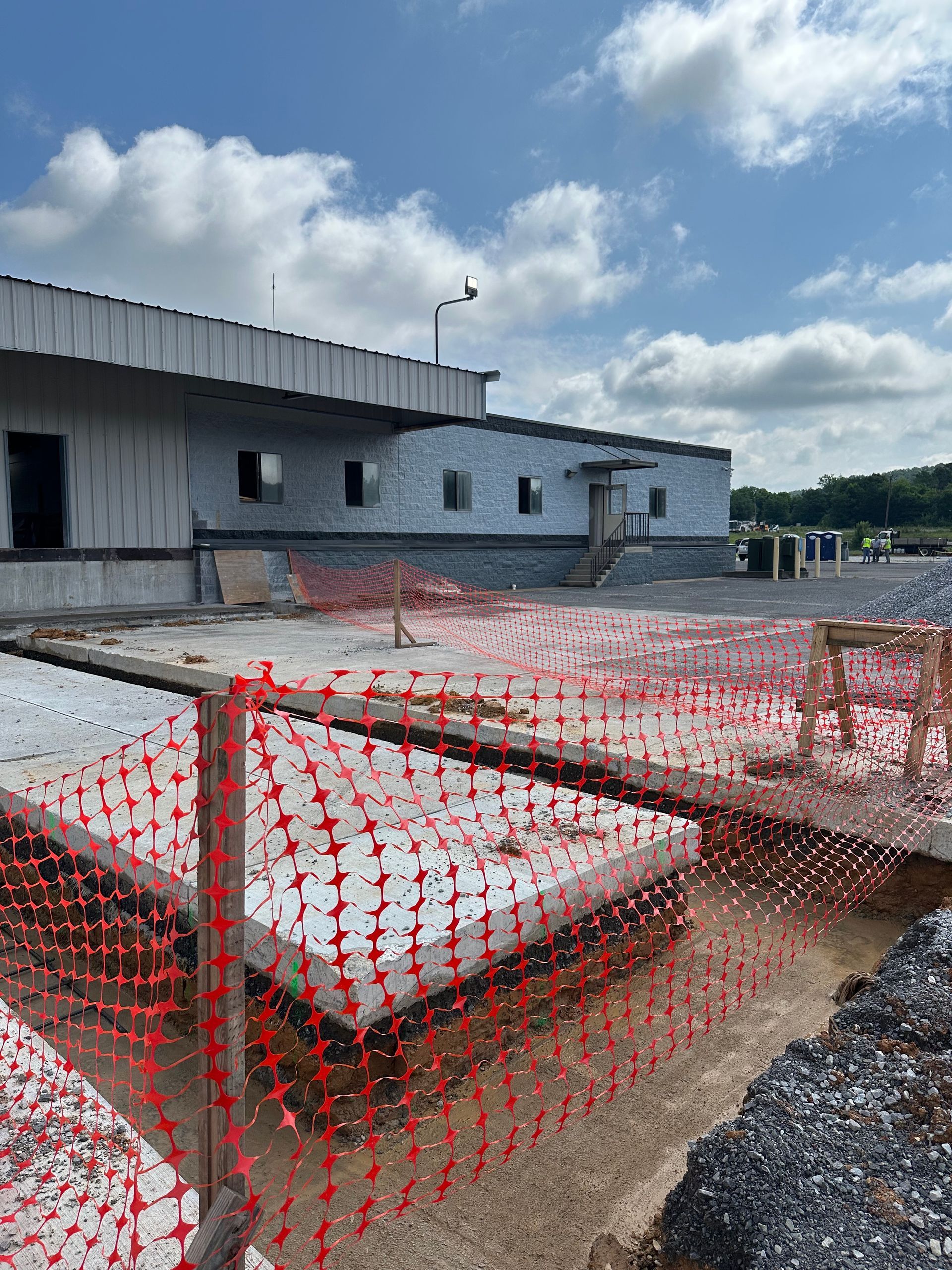 Construction site with red safety fencing, concrete blocks, and an unfinished gray building under a cloudy sky