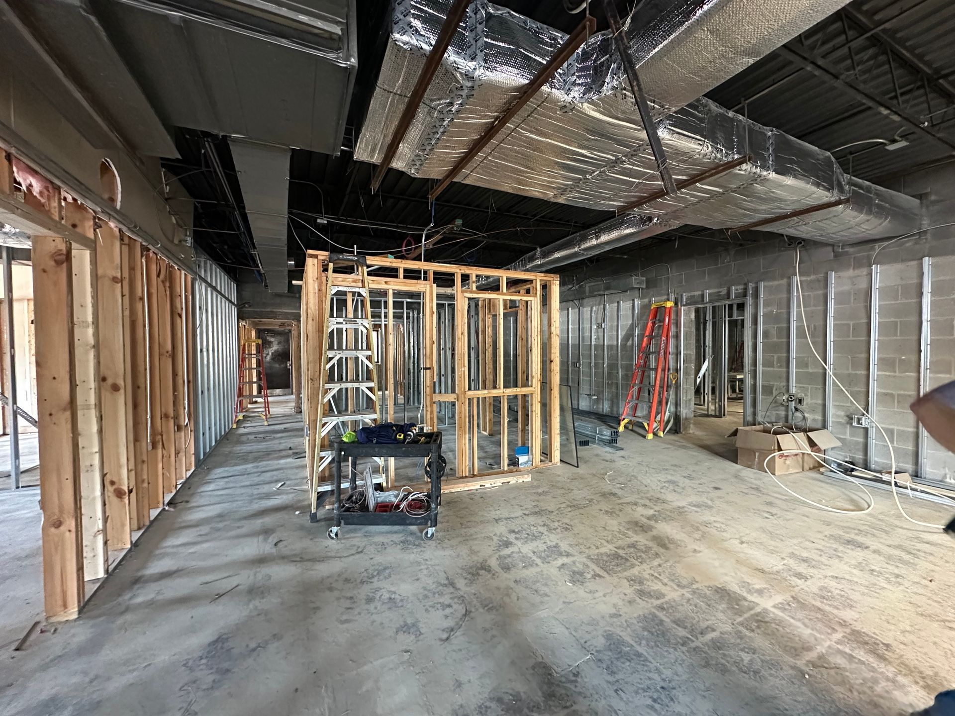 Interior of a construction site with exposed framing, insulation, ladders, and unfinished floor and ceiling panels