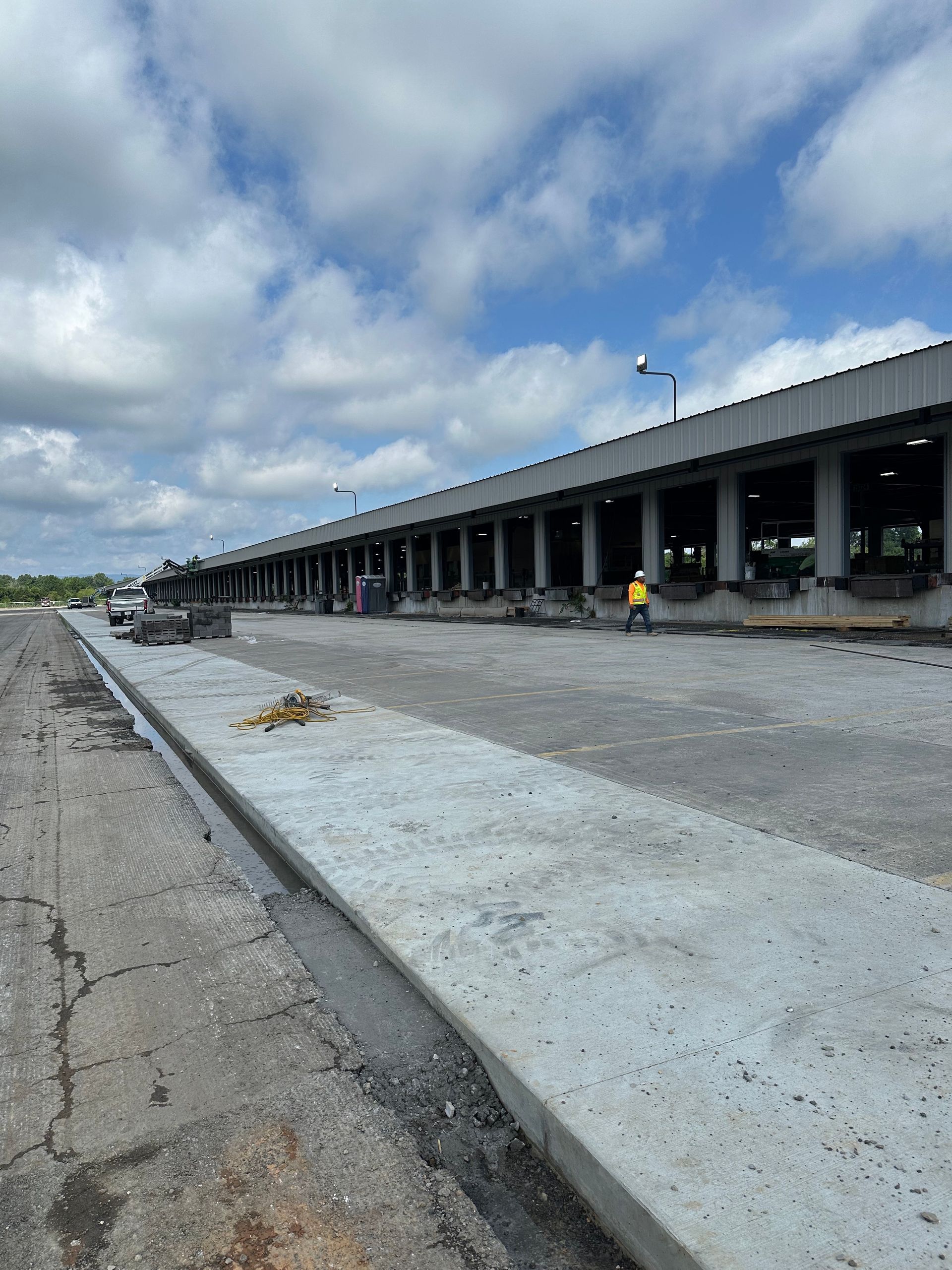 Long warehouse loading dock under construction beside a cracked road, with scattered debris and cloudy sky