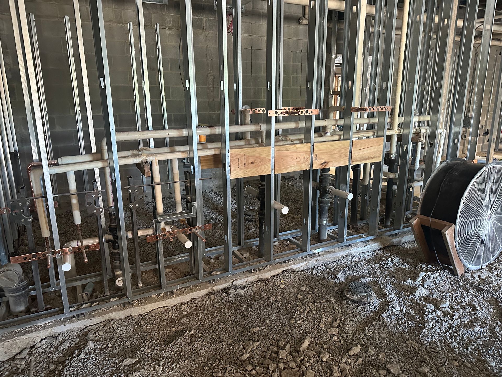 Construction site with exposed wall studs, support beams, and a dirt floor with debris.