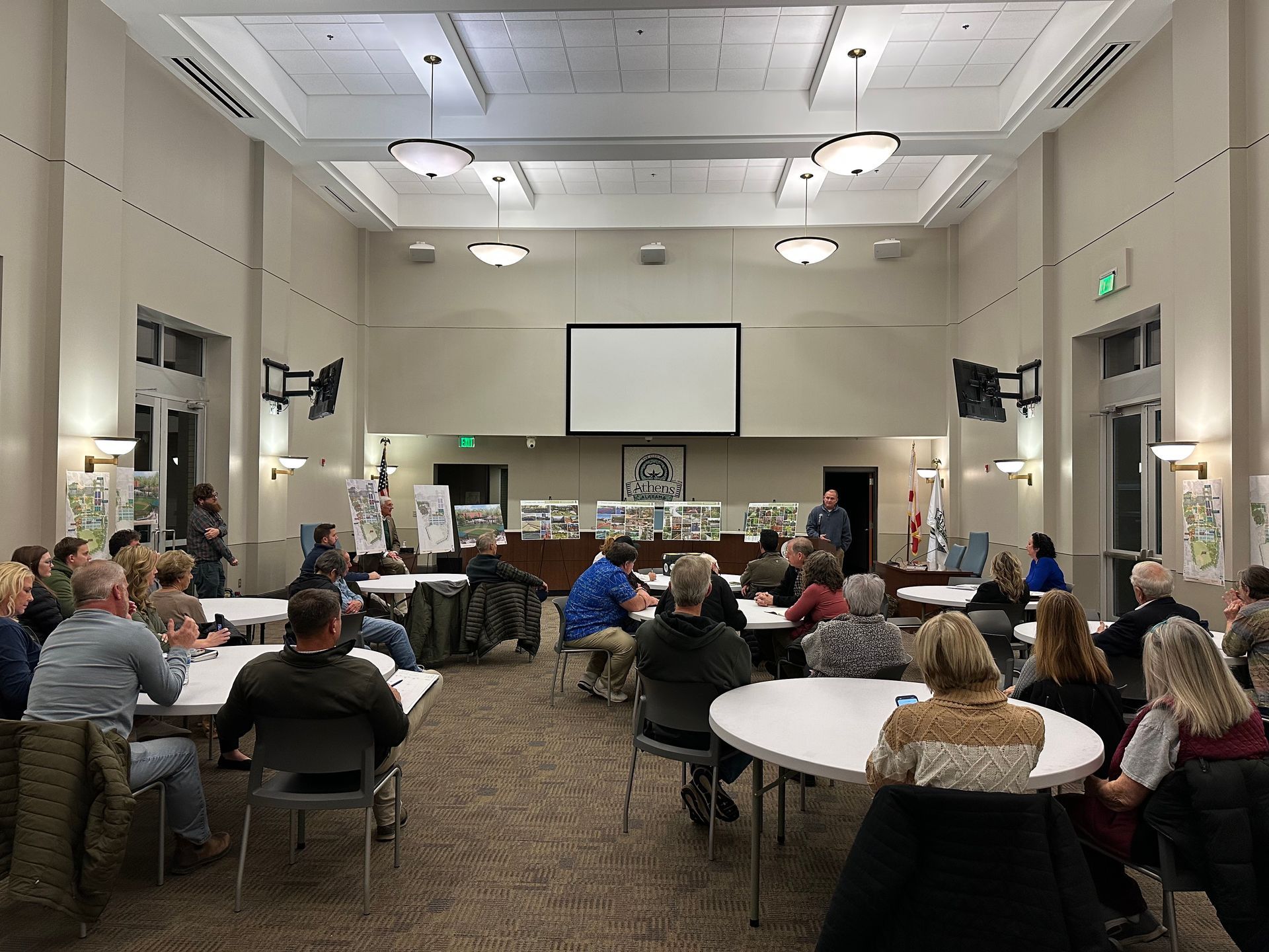 Conference room meeting with people seated around tables facing a presentation screen