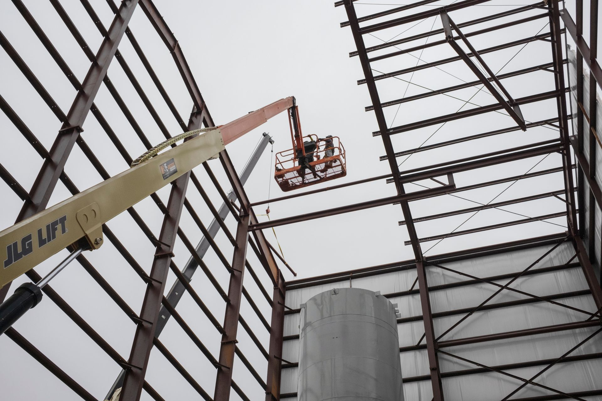 Steel frame building under construction, worker in lift welding overhead.