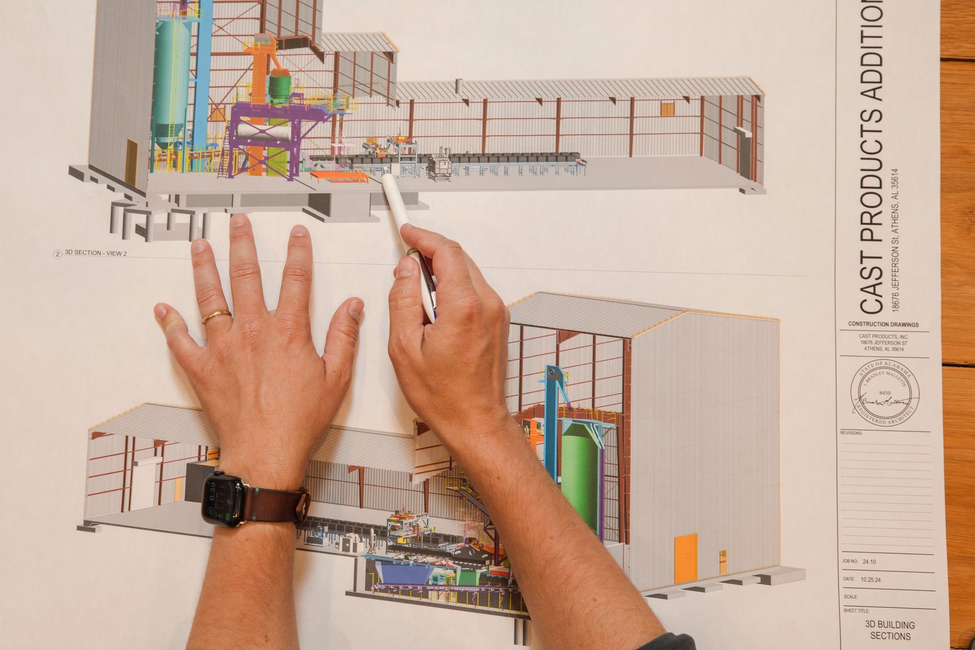Hands pointing at an architectural rendering of a factory addition, detailing machinery and construction.