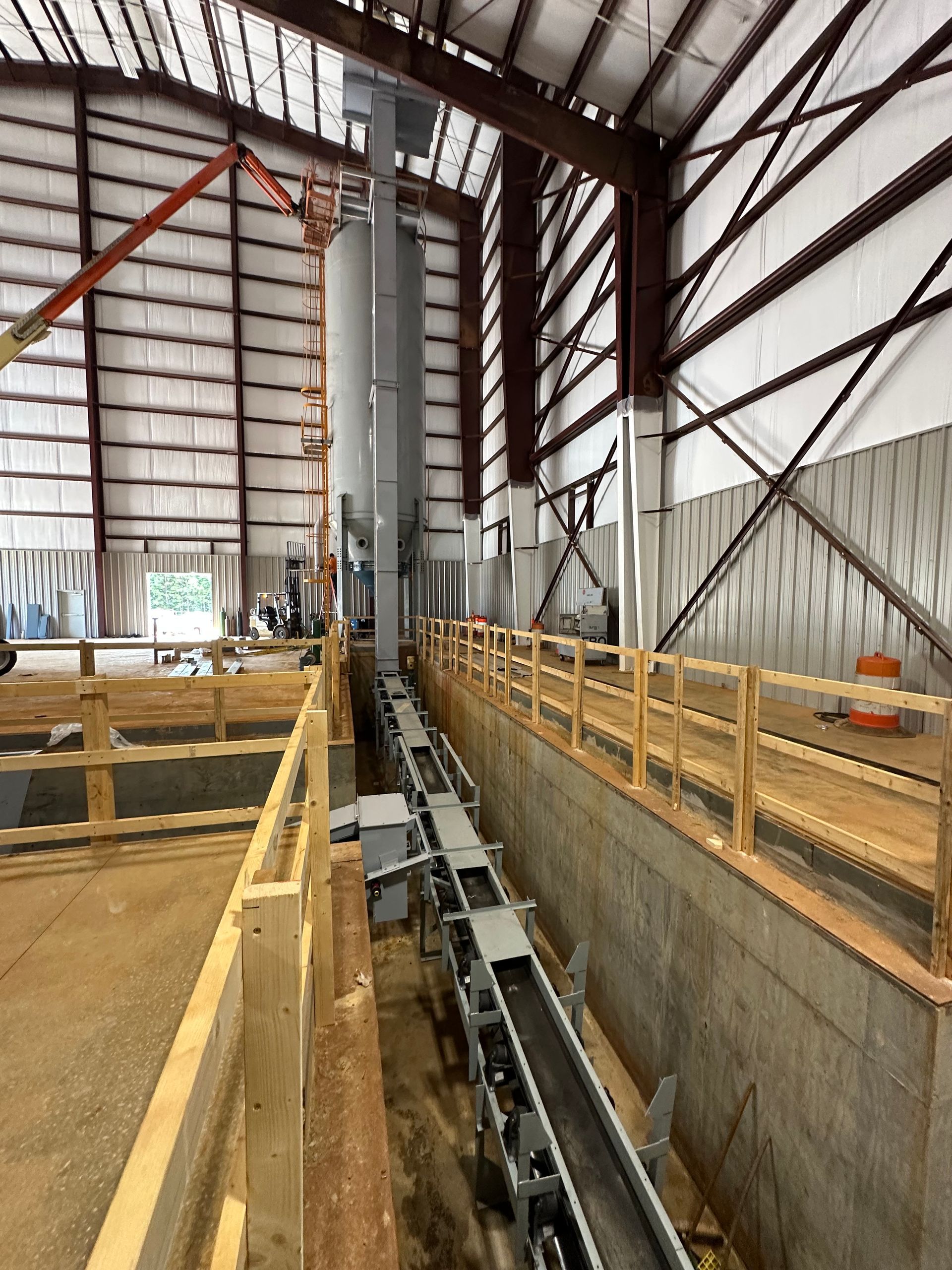 Construction site with conveyor belt, silo, and wooden structures inside a warehouse.