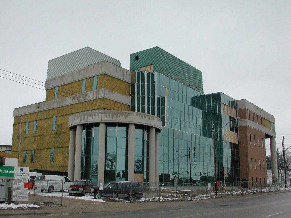 Modern multi-story building with glass facade and cylindrical entrance, overcast sky.