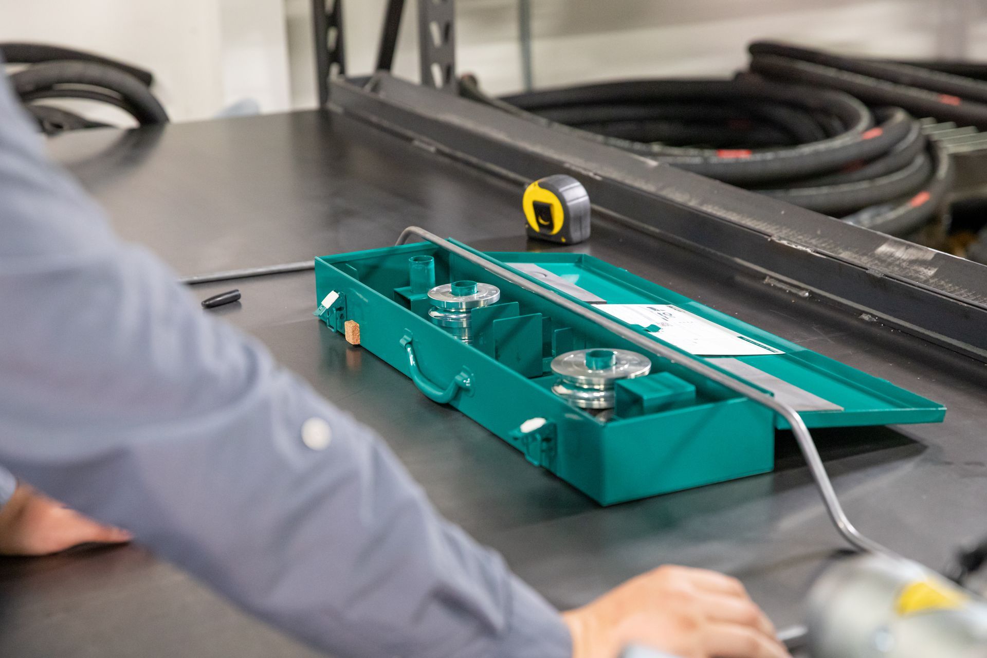 A man is working on a hydraulic hose with a toolbox on a table.