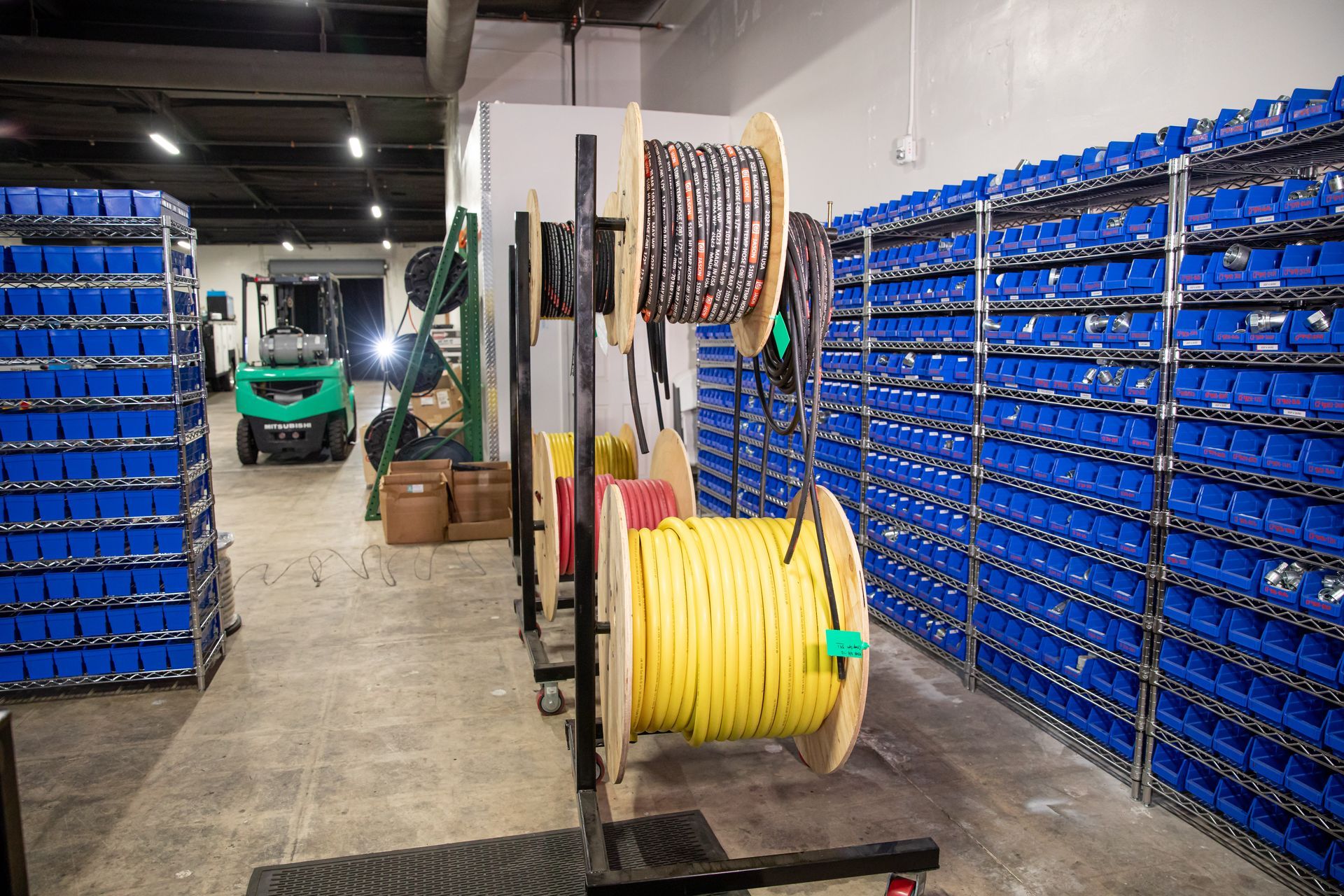 A warehouse filled with lots of blue bins and spools of hydraulic hoses.