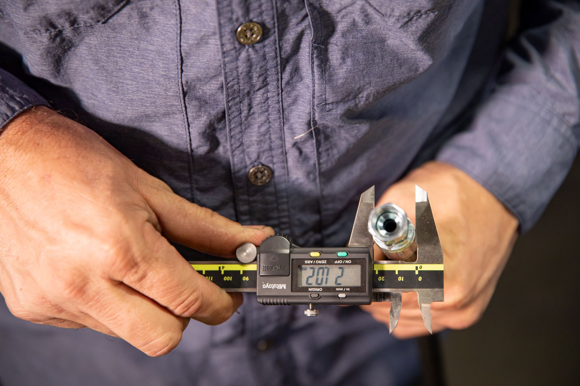 A man is measuring a hydraulic hose with a digital caliper.