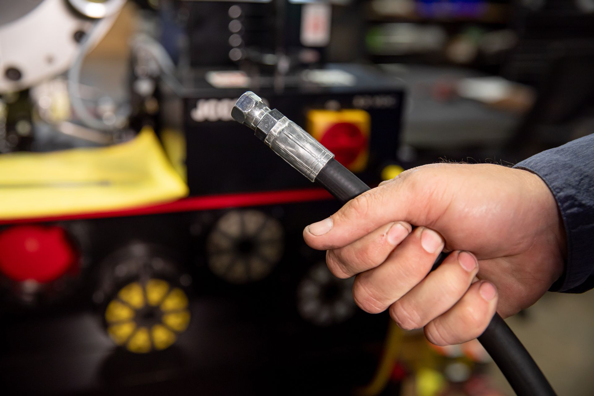 A person is holding a hydraulic hose in their hand in front of a machine.