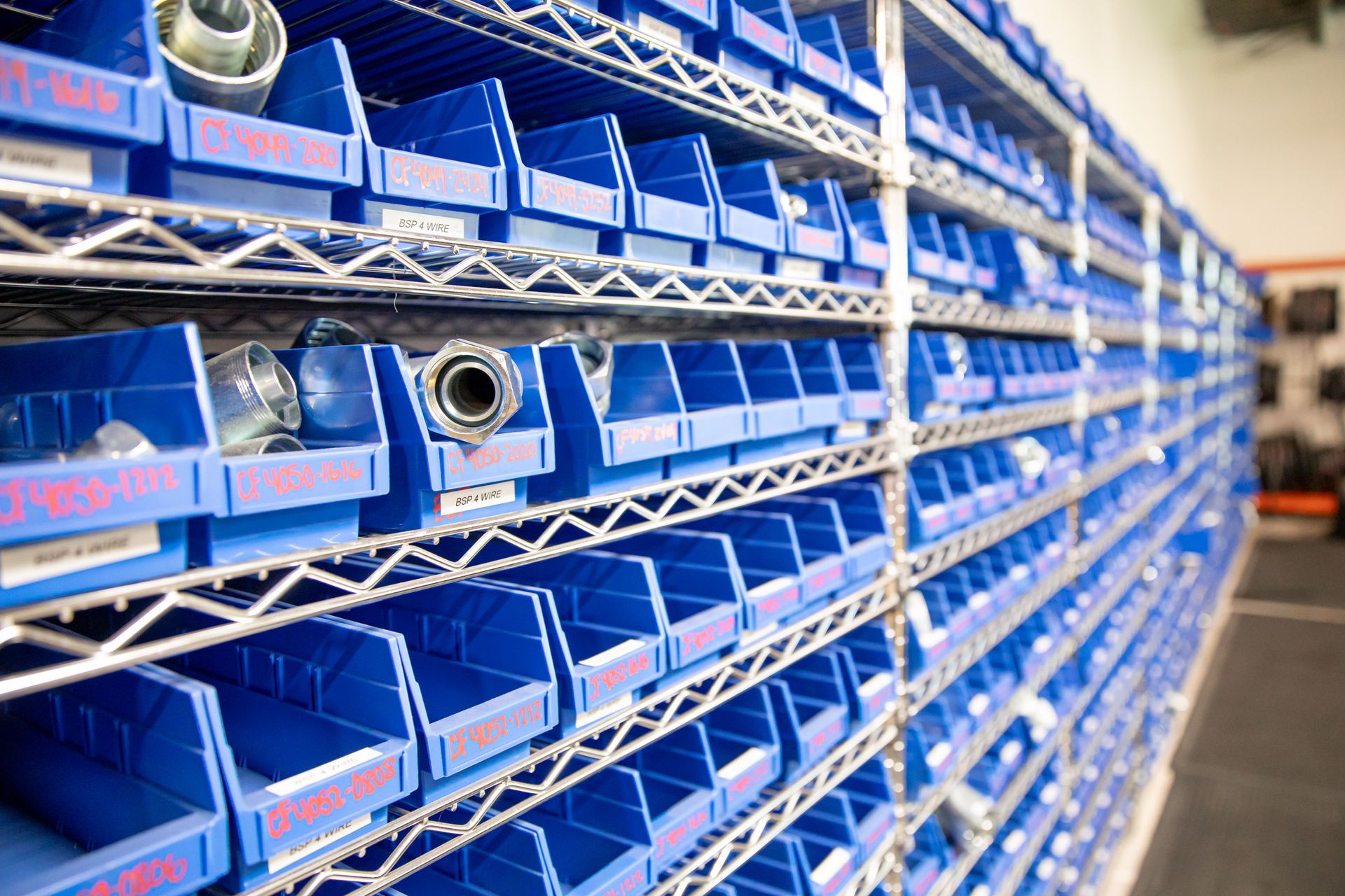 A warehouse filled with lots of blue bins and parts for hydraulic and industrial hoses.