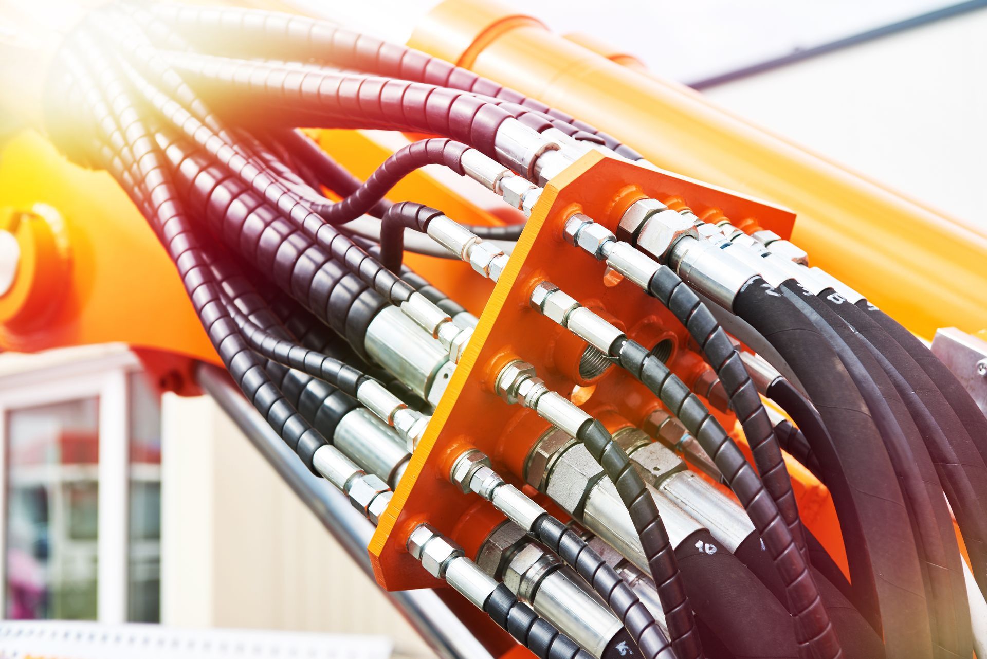 Close-up of orange hydraulic hoses and metal connectors on heavy machinery.