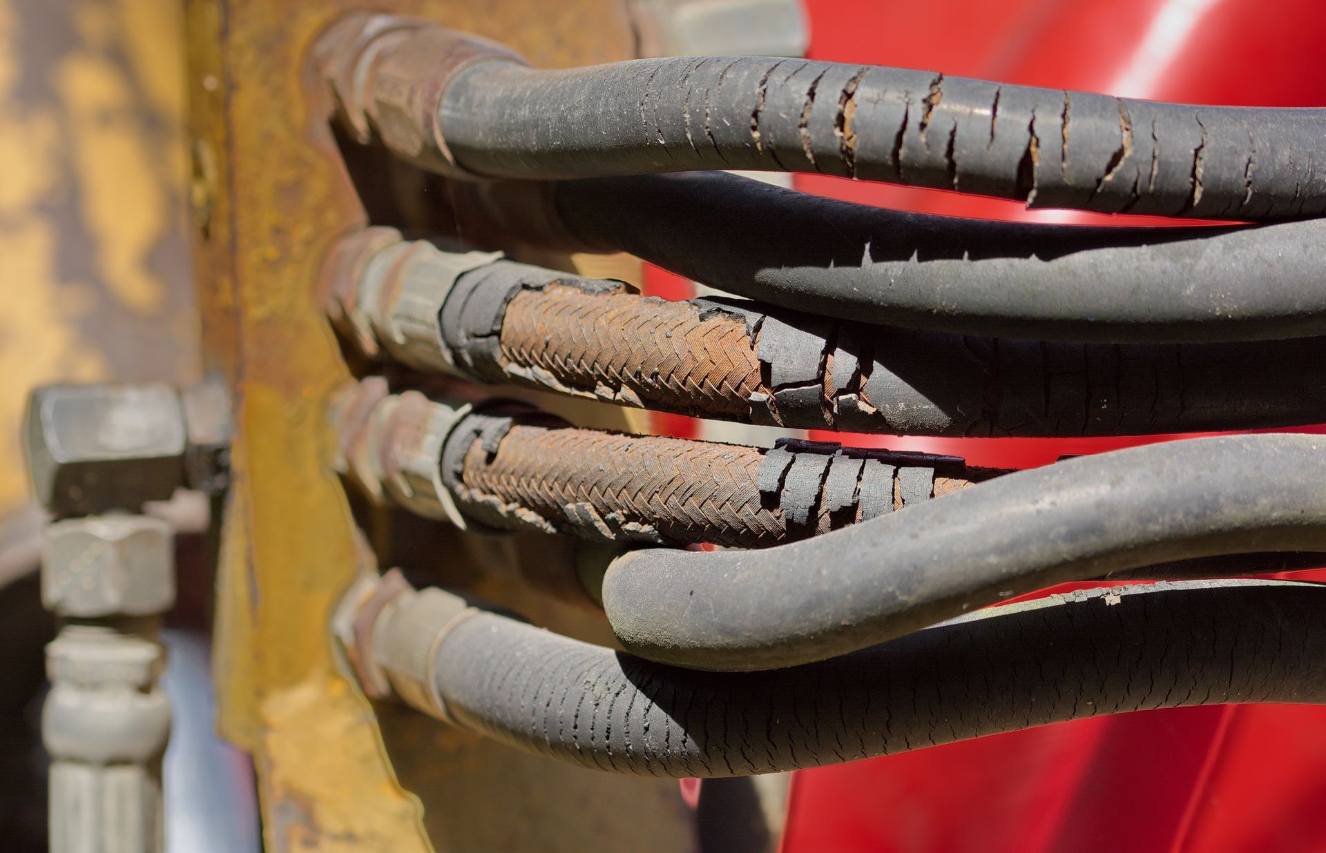 A closeup of a bunch of rusting hydraulic hoses with their covers peeling off attached to a machine.