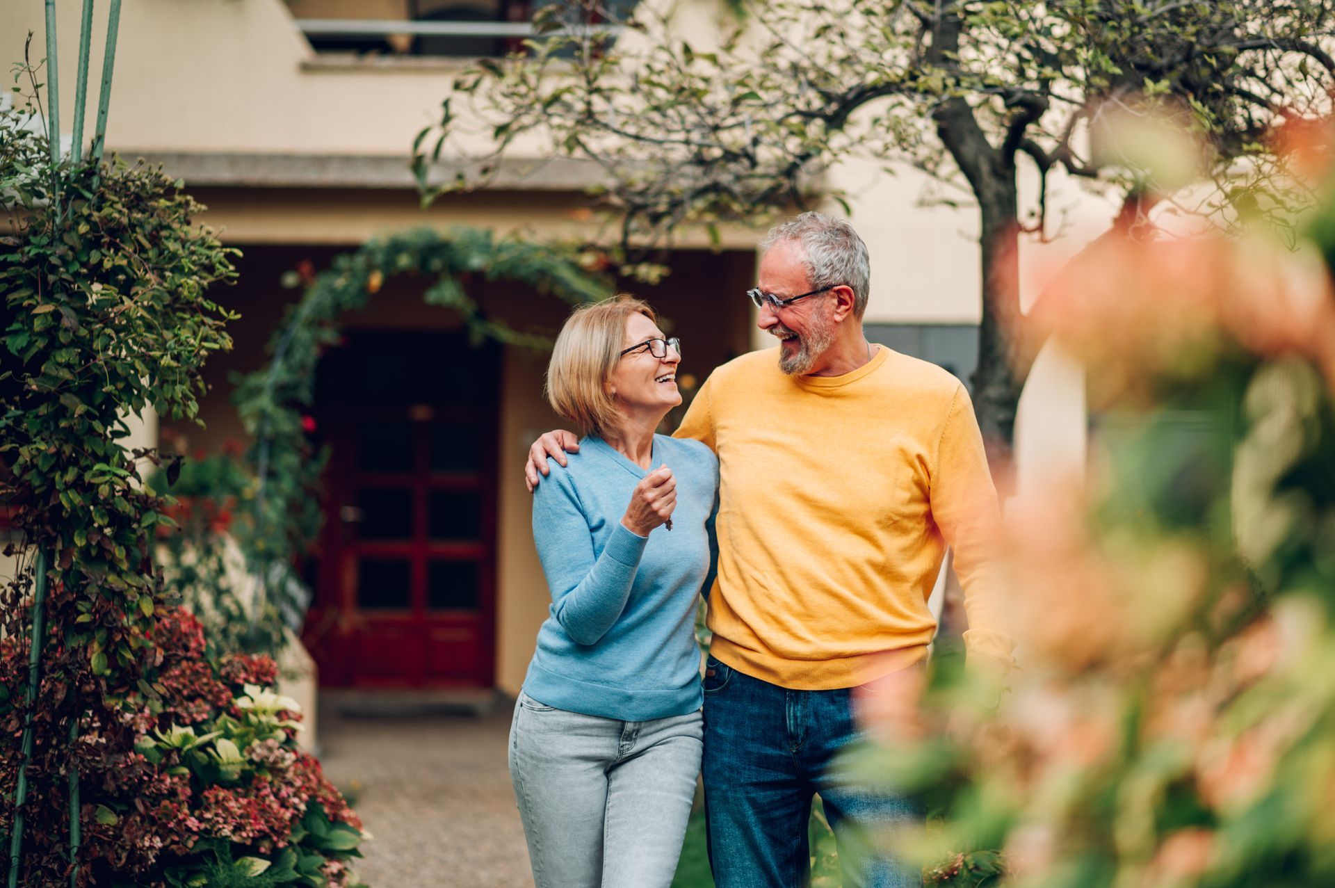 Smiling couple walking arm in arm in a garden courtyard, with a house and trees in the background
