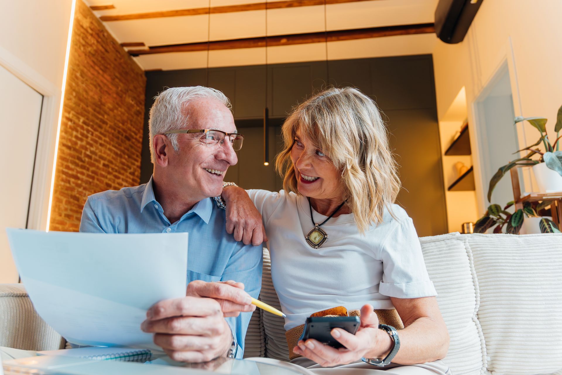 Smiling couple sitting on a couch, reviewing papers together in a bright living room.