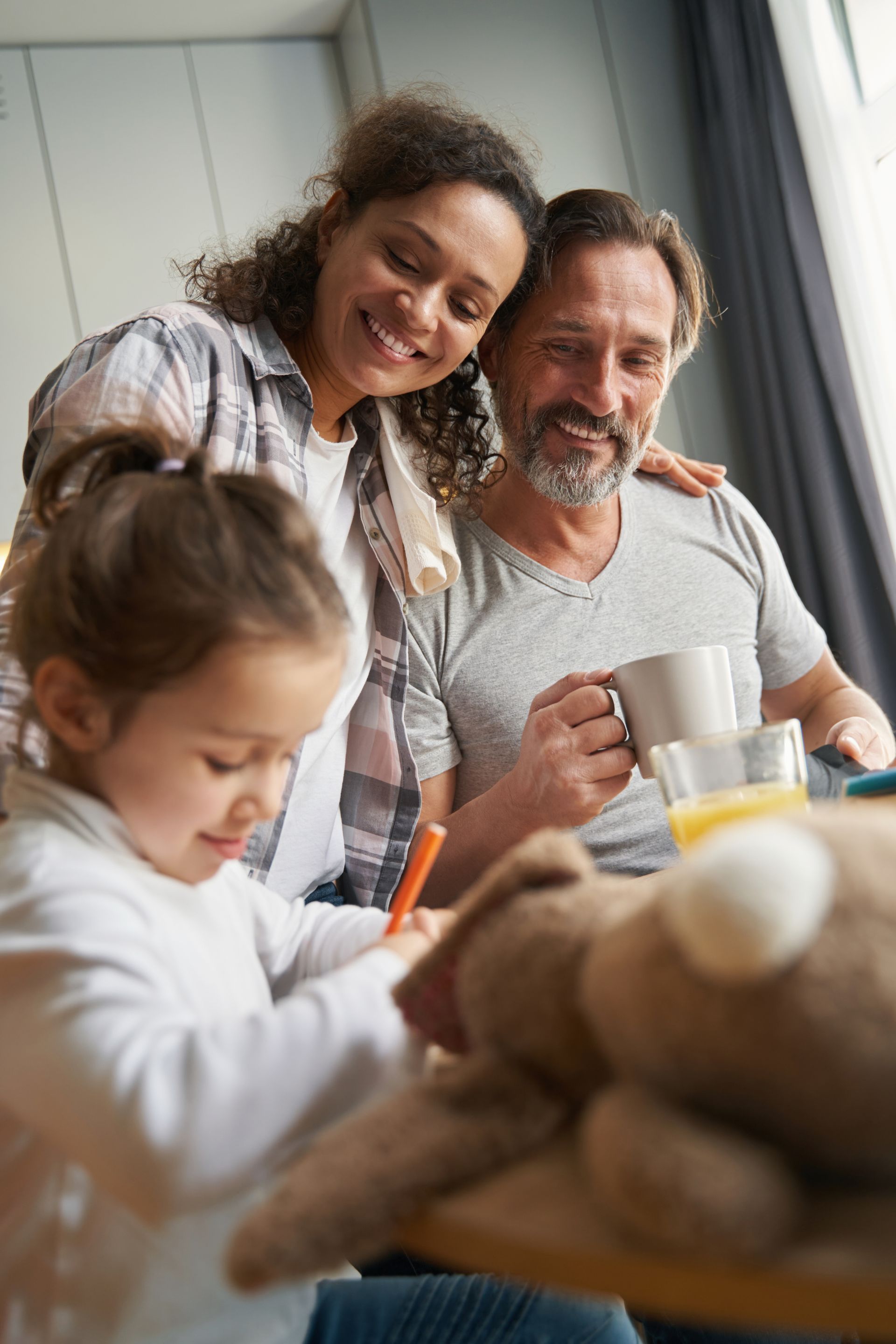 Family gathered at a table, smiling while a child draws in the foreground