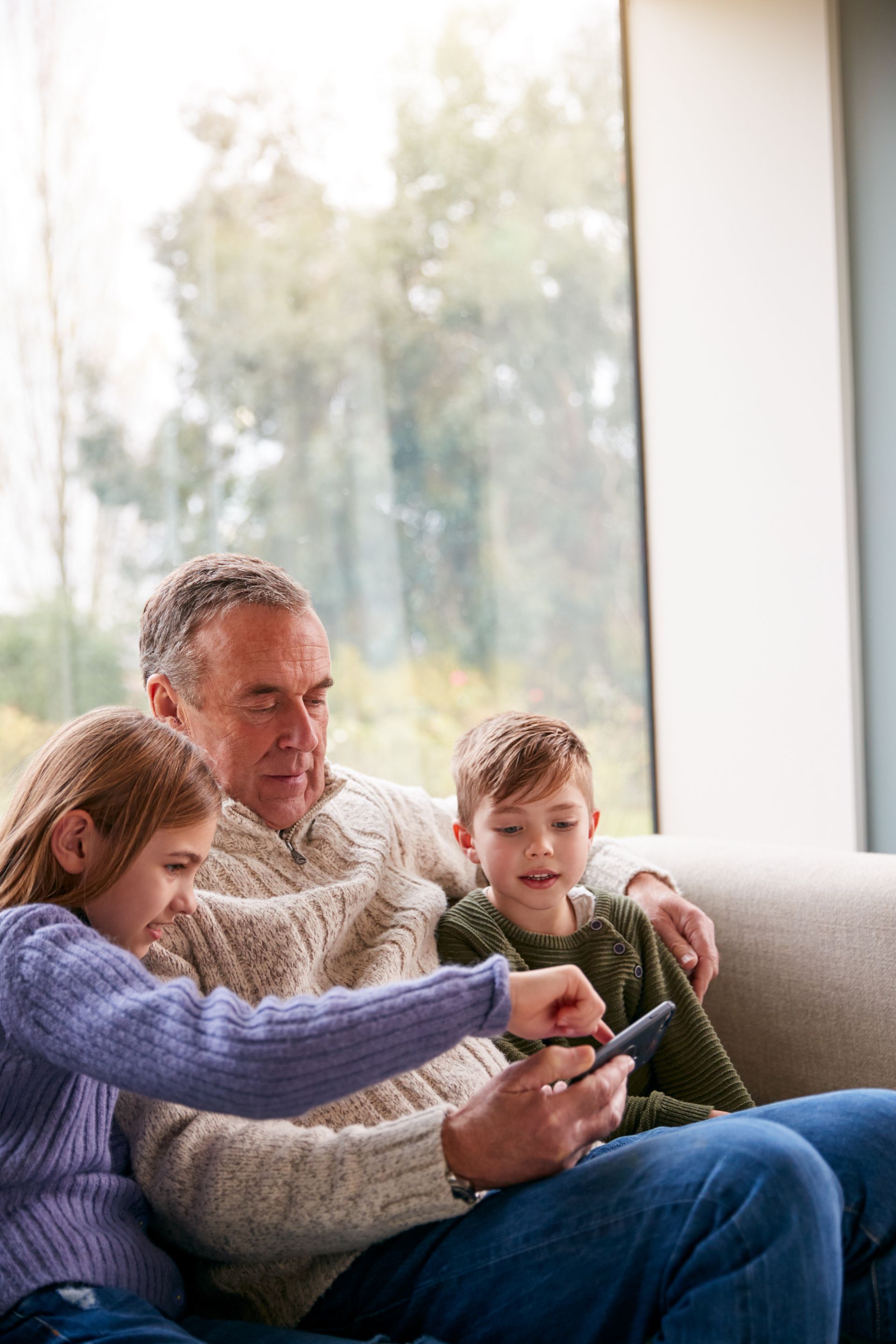 Three people on a couch using a tablet by a bright window