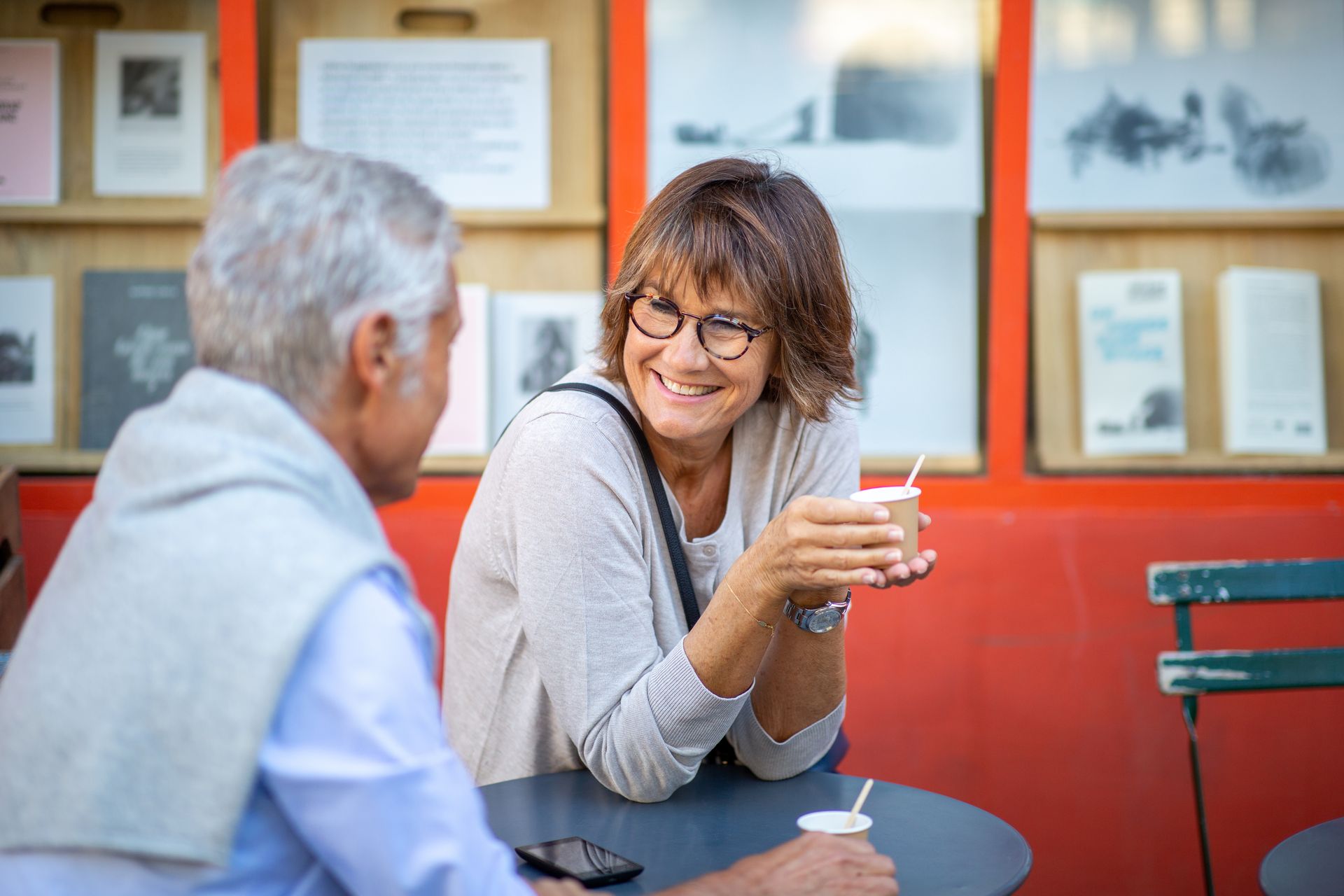 Two people chatting at a café table, one holding a drink and smiling